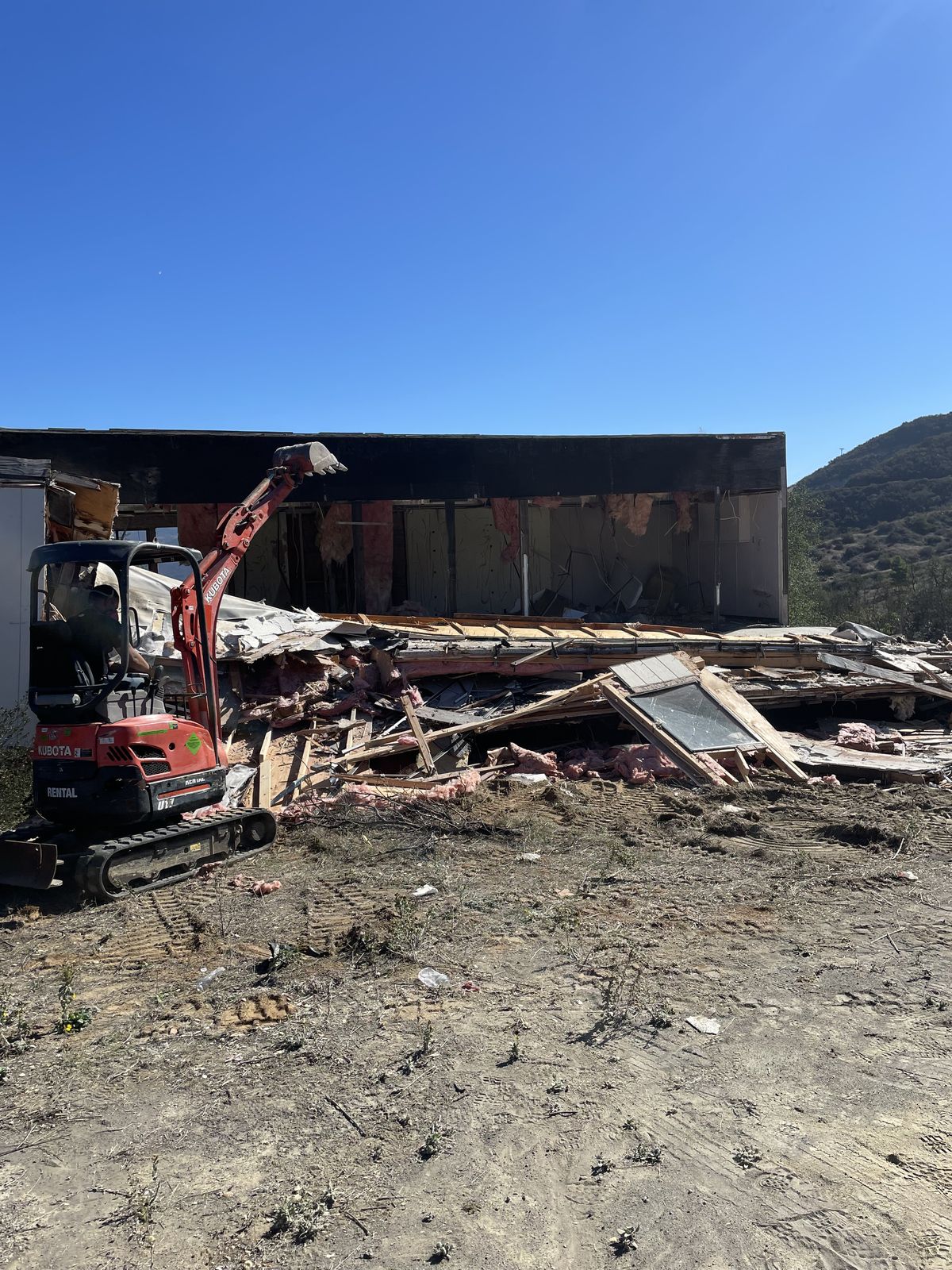 Excavator tearing down a wooden structure during a demolition in San Diego County