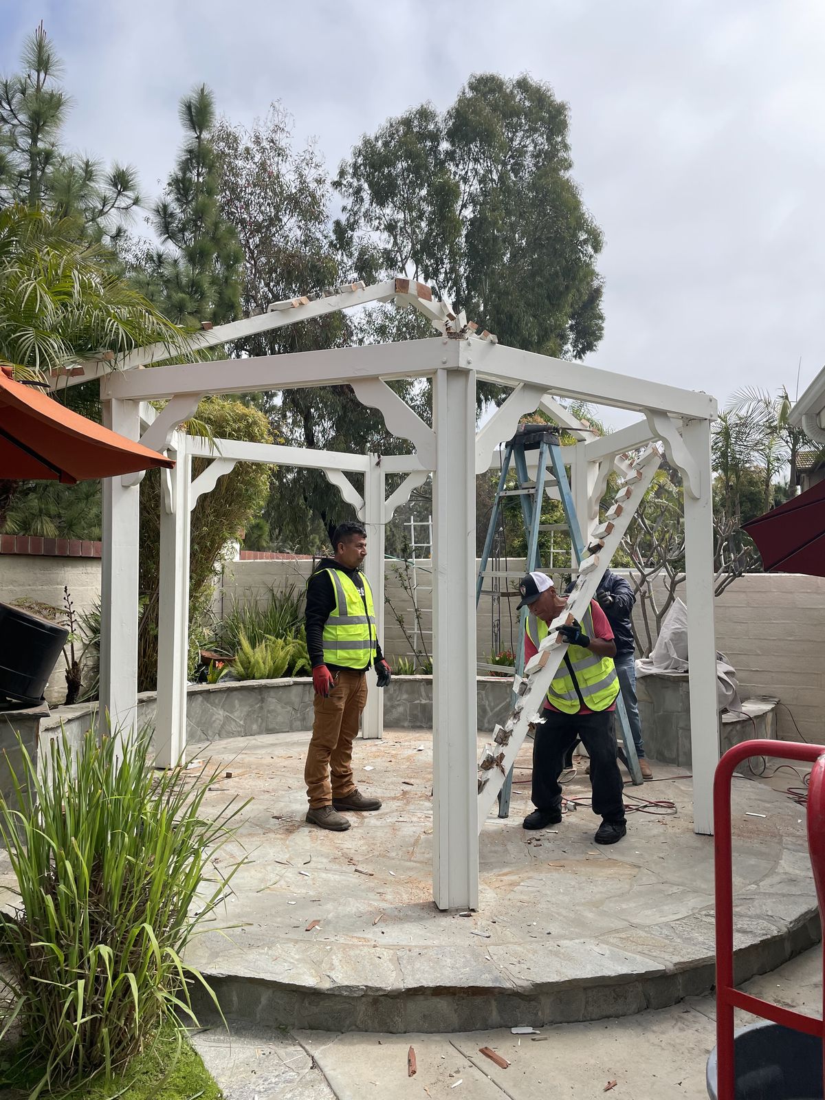 Crew dismantling large white pergola structure